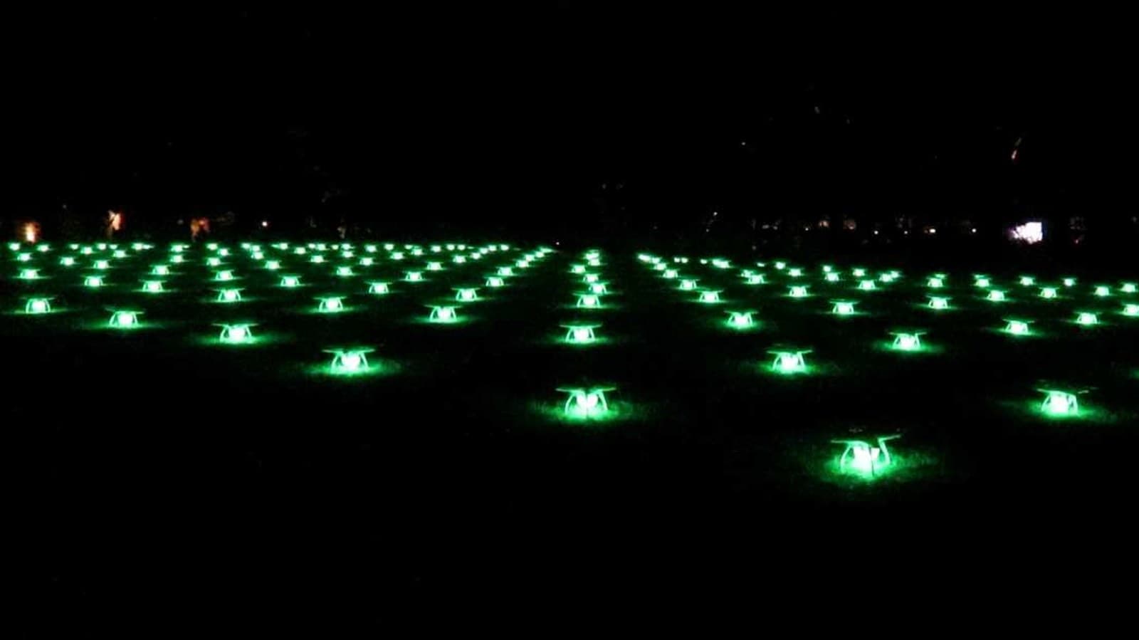 Coordinated drone formation glowing green at night — autonomous mission execution at scale.